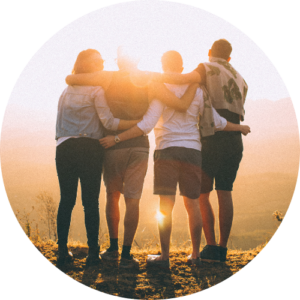 Vier Menschen stehen nebeneinander und halten sich im Arm. Sie schauen in den Sonnenaufgang und sind auf dem Bild nur von Hinten sichtbar